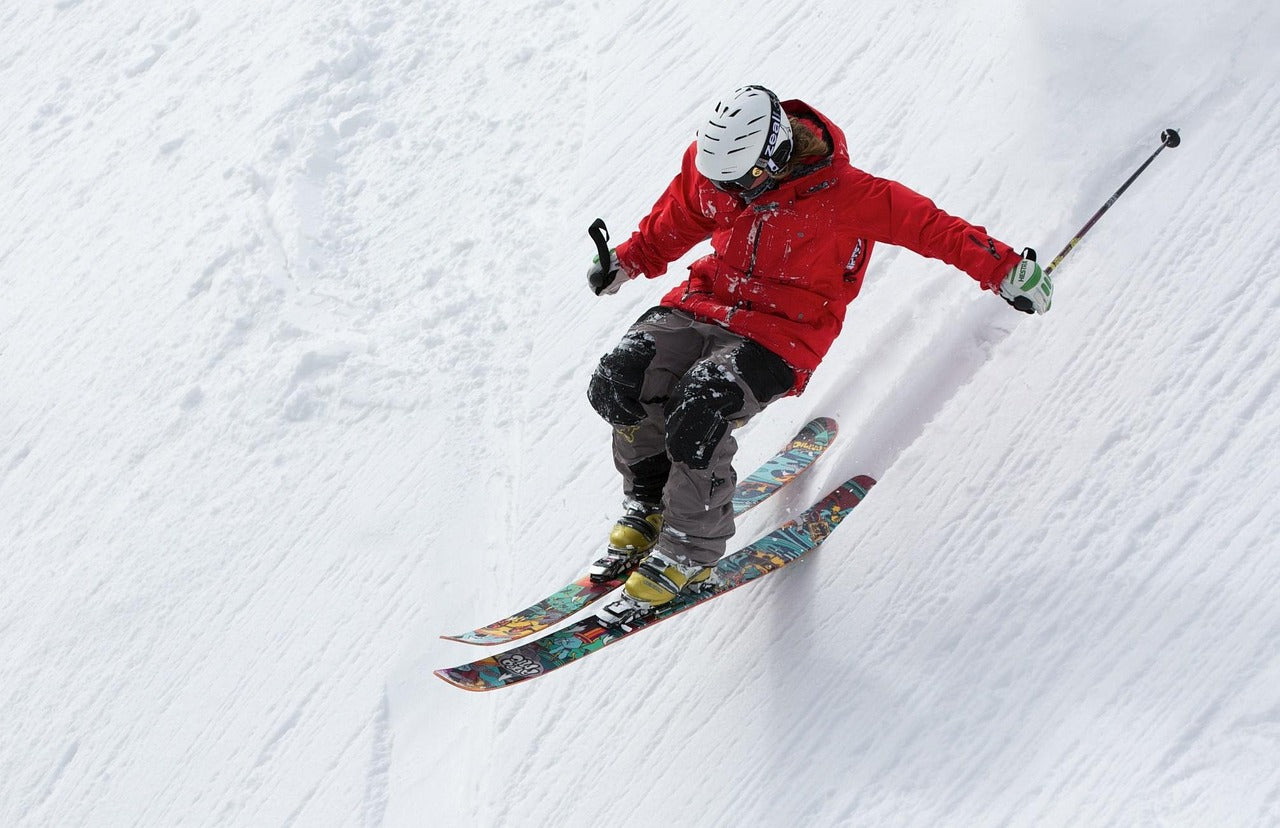 Person skiing down a snowy slope wearing a red jacket and helmet.